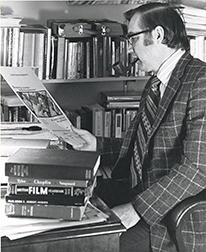 Photograph of Norman Keim Sitting at a Desk Holding Film Poster
