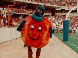 Mascot in a large orange costume, later called Otto, dated 1982 on sideline of Syracuse University stadium football field