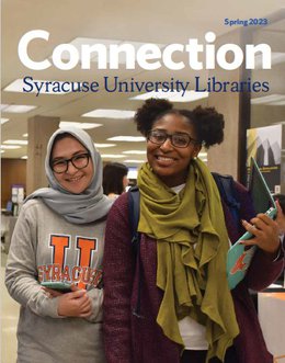 two students smiling, one on left wearing scarf over head and Syracuse U sweatshirt, one on right carrying laptop